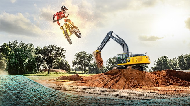 A motocross racer soars through the air as John Deere 350G LC SmartGrade™ Excavator is shaping one of the jumps on the course.