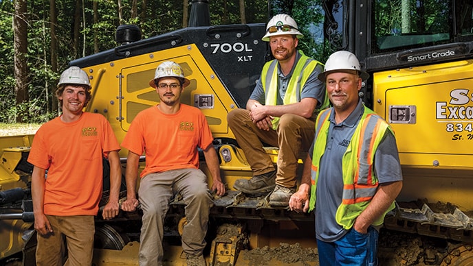 Dylan Nussbaum, Colt Nussbaum, Cody Nussbaum, and Jesse Nussbaum pose near a John Deere 700L XLT SmartGrade Crawler Dozer.