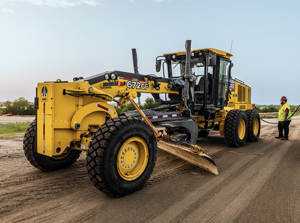 Stefan stands beside a John Deere 672GP Motor Grader and refuels the machine. 