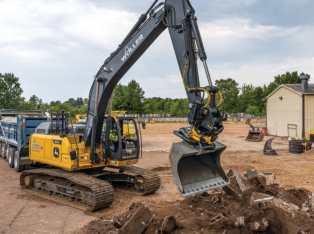 A 210G LC SmartGrade Excavator with an engcon EC-Oil coupler and Tiltrotator attachment lowers its bucket and moves materials.