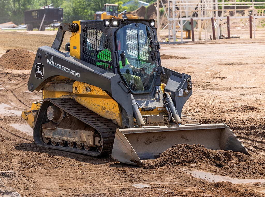 A 333G CTL levels dirt on a jobsite in Wisconsin as a pair of other John Deere machines work in the background.