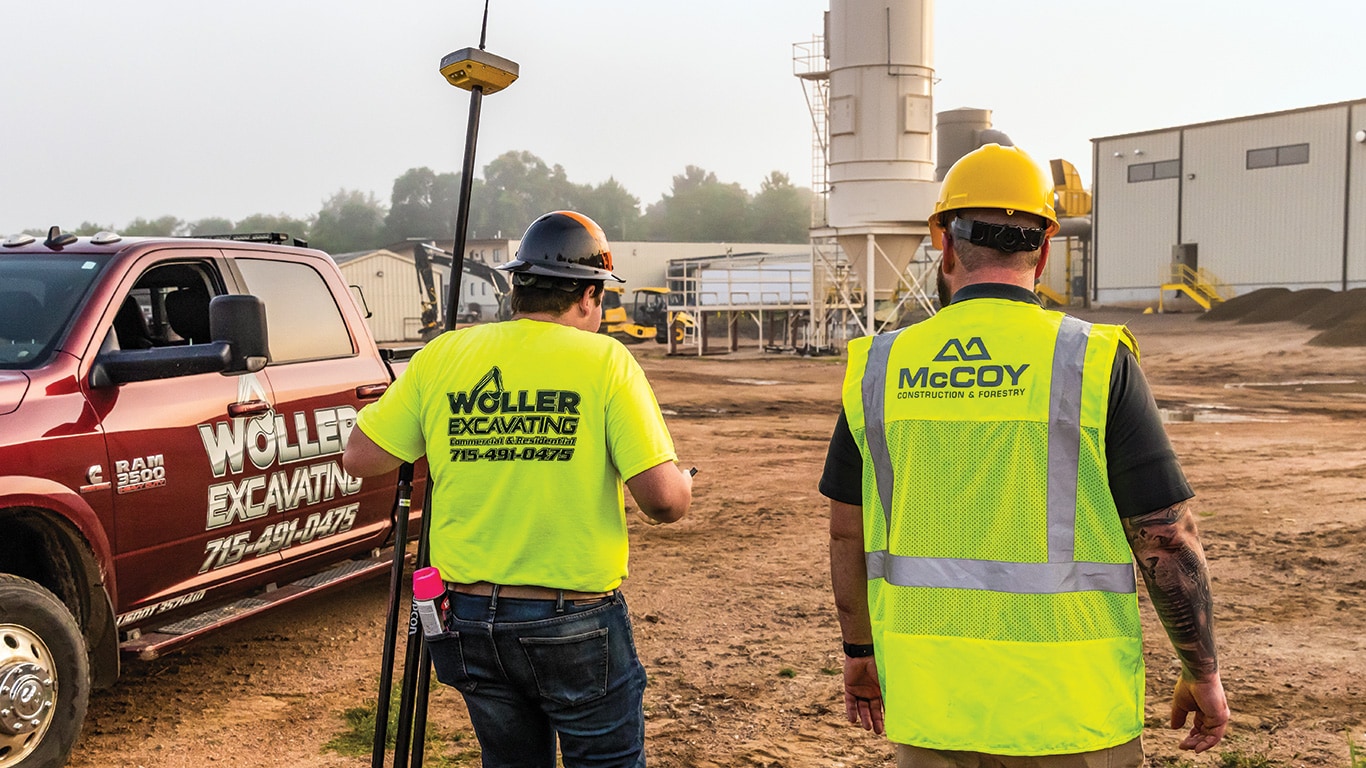 Brett Woller carries a Topcon positioning system receiver attached to a tripod as he walks alongside Taylor Long.