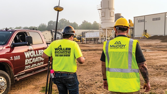 Brett Woller, owner of Woller Excavating, carries a Topcon positioning system receiver attached to a tripod as he walks alongside Taylor Long, a product support technology representative for McCoy Construction & Forestry.