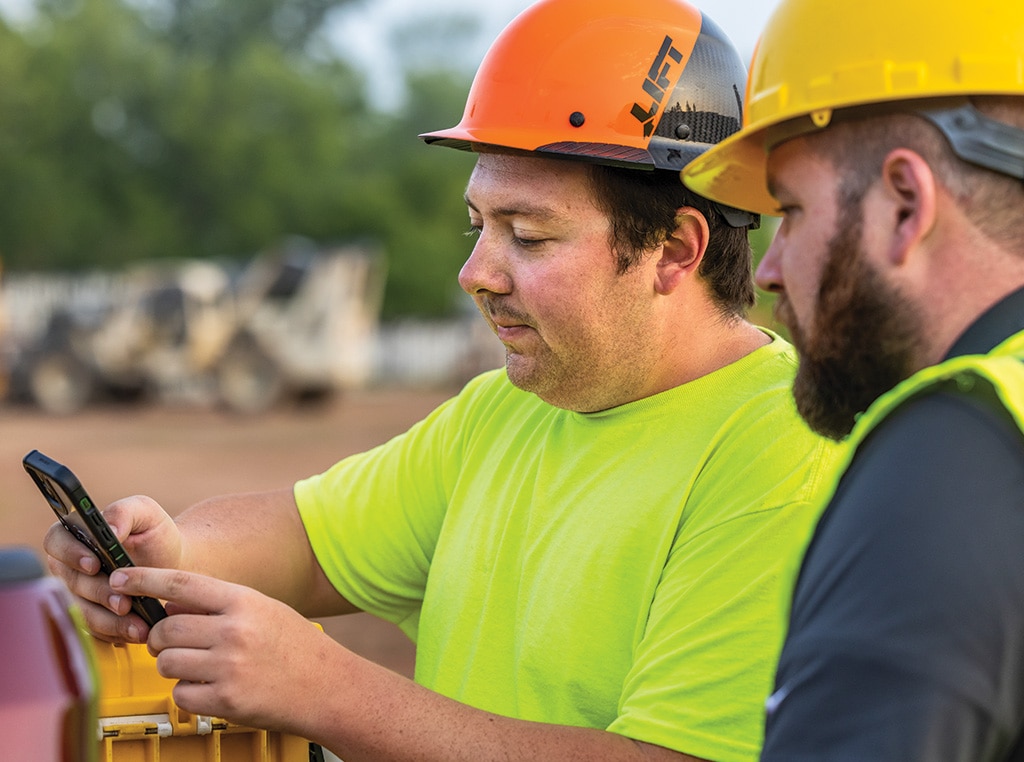 Brett holds his mobile phone as Taylor looks over his shoulder and advises him on setting up the John Deere Operations Center app.