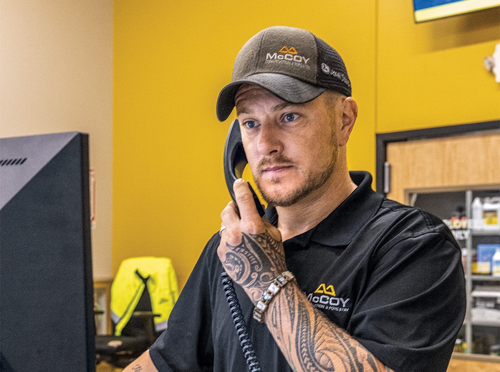 Seth stands at his computer with a phone to his ear and discusses equipment maintenance needs with a customer. 