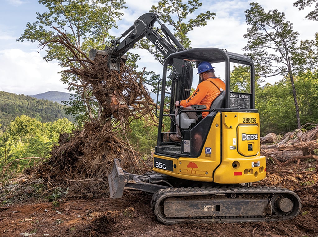A 35G Compact Excavator picks up a brush pile and removes it from a jobsite. 