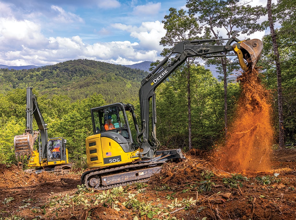 A 50G Compact Excavator unloads dirt, while a 135G Excavator digs into a pile on a jobsite.