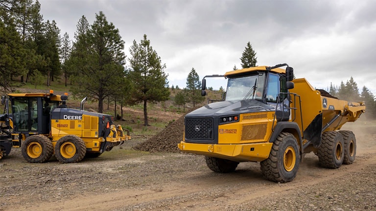 two trucks on a construction site with trees in background