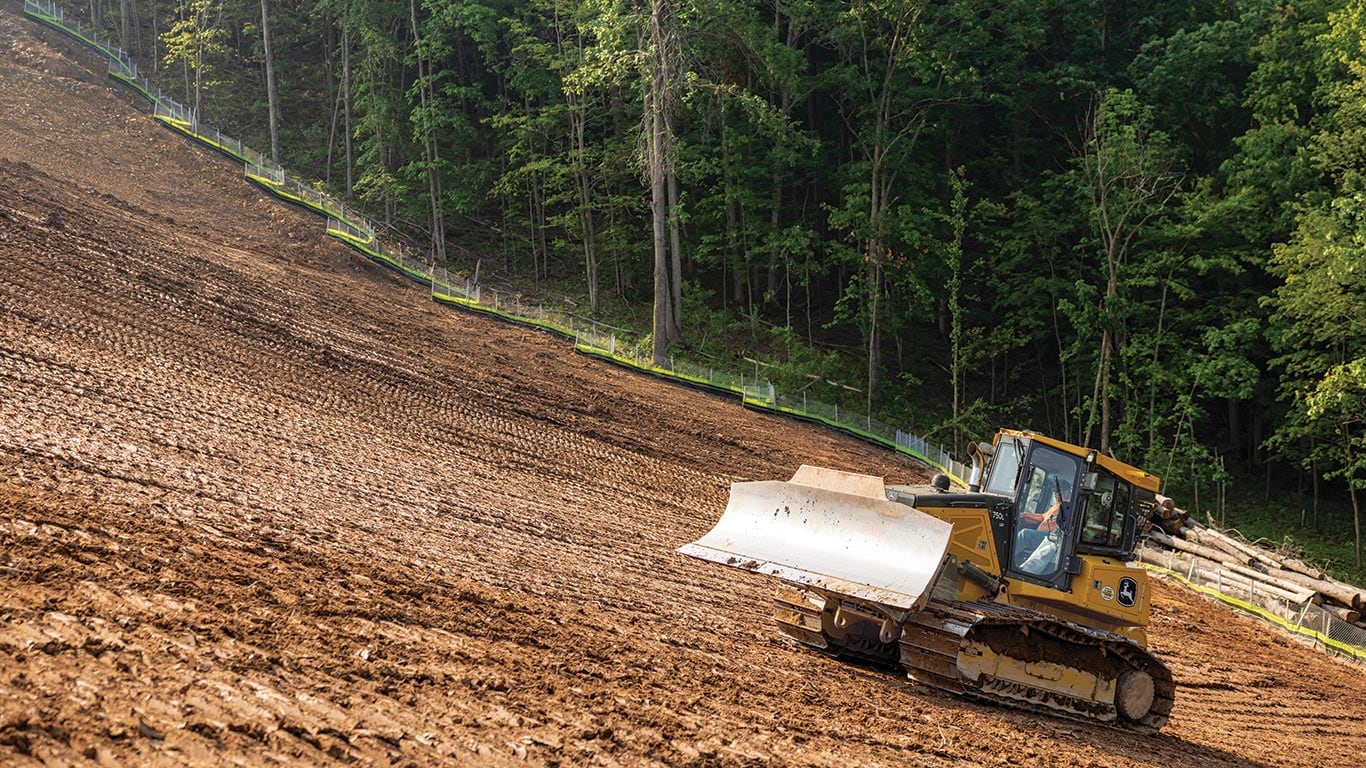 A John Deere 750 L-Tier Dozer moves into position up hill to level and grade dirt.