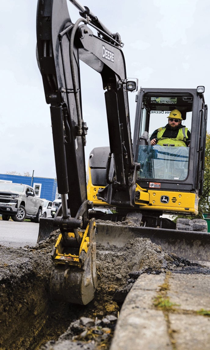 An operator drives a mini excavator on a jobsite