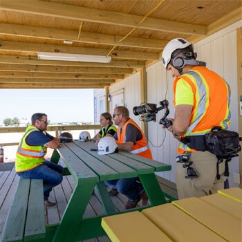 A woman with long blonde hair, wearing a black jacket, poses against a soft-focus dark background.