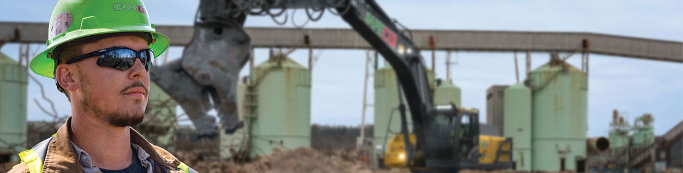 Dustin wearing a green hard hat and sunglasses in front of a tractor