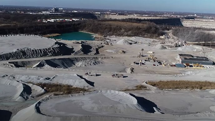 Four employees with their backs to the camera watch a John Deere 380G LC Excavator, a 460E Articulated Dump Truck, and an 872 GP SmartGrade Motor Grader work at moving dirt.