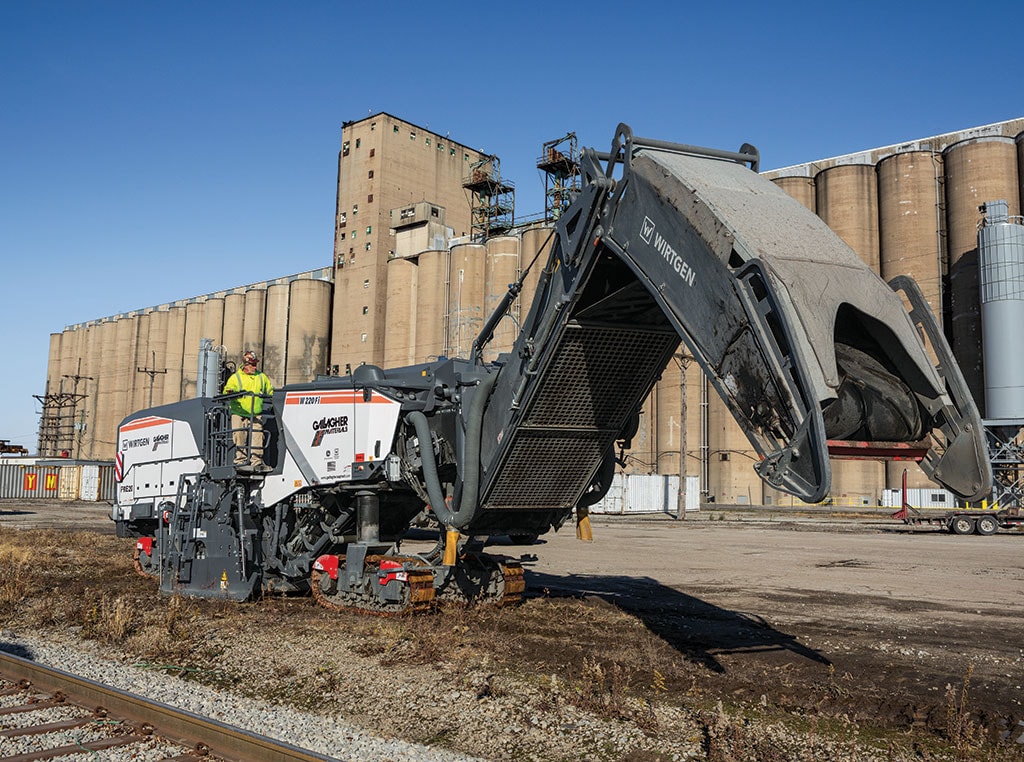 A Wirtgen W220Fi cold milling machine working in front of a large factory building