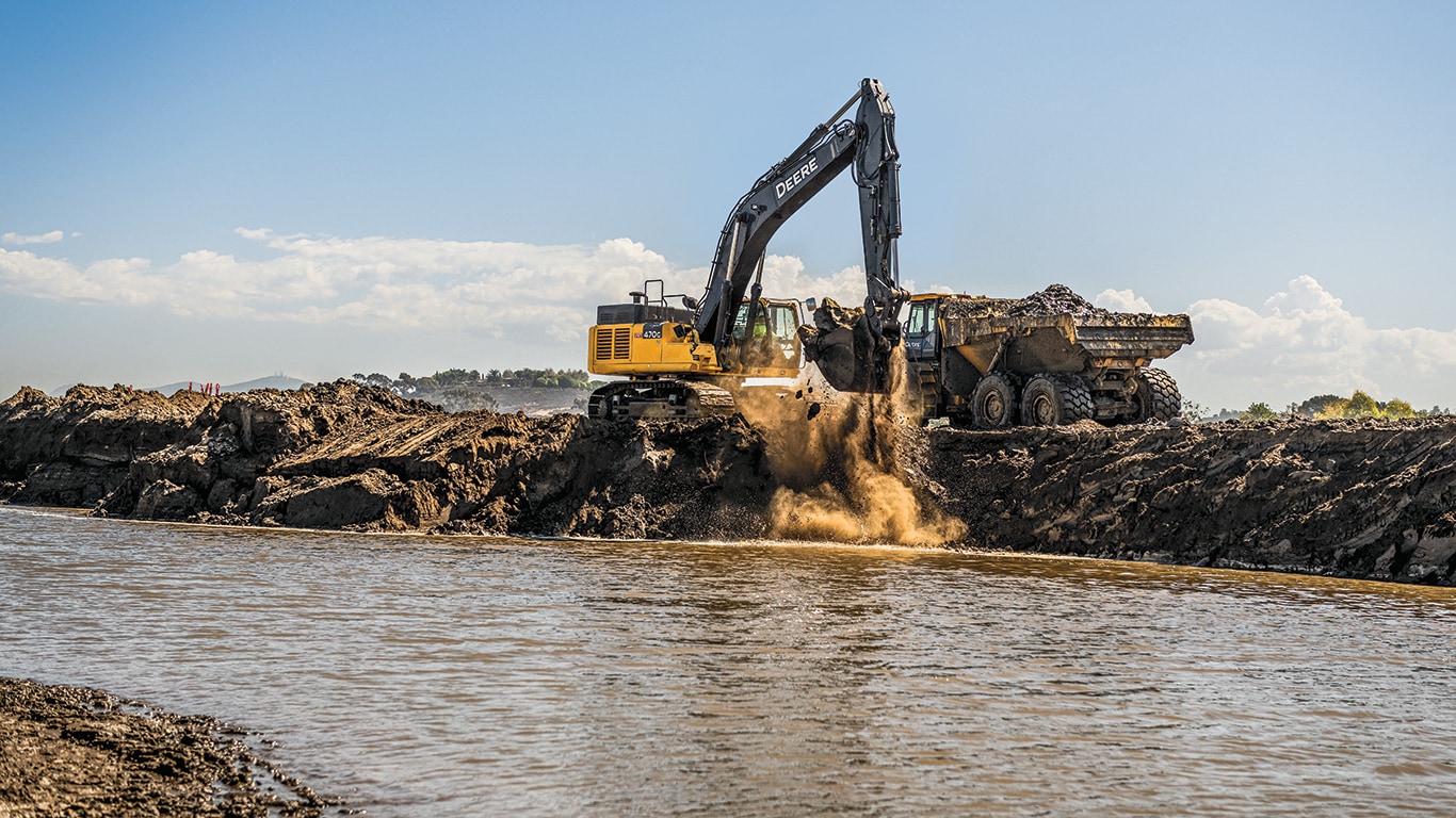 A John Deere 470G LC Excavator is moving a bucket full of dirt from a lagoon to be dumped into a 410E-II Articulated Dump Truck.