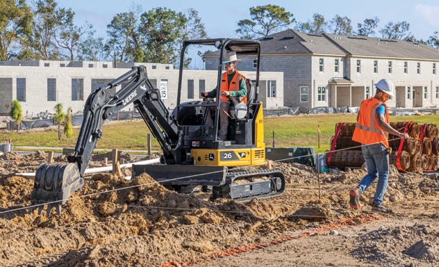 The bucket of a John Deere 26P-Tier Compact Excavator extends to start digging into the ground