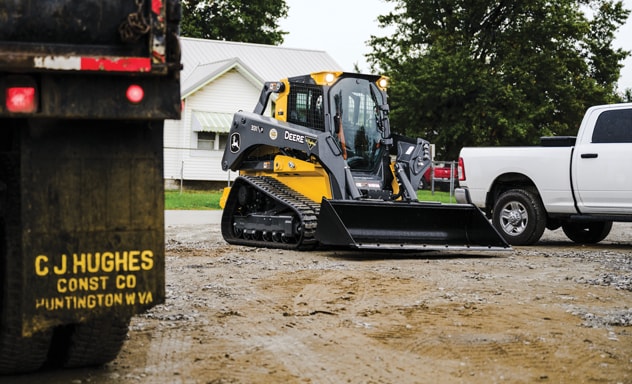 The lights of the John Deere 331P Compact Track Loader shine brightly in the morning dawn.