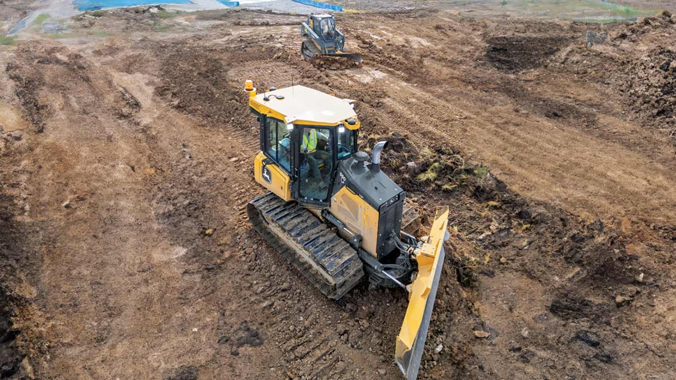 Two bulldozers leveling dirt at a construction site, one in the foreground with visible operator.