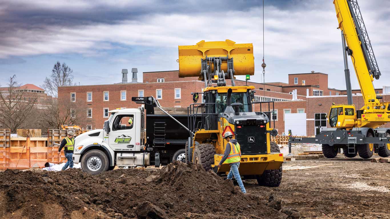 Construction site with workers, dump truck, crane, and front loader moving dirt.
