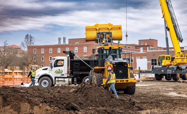 Construction site with workers, dump truck, crane, and front loader moving dirt.