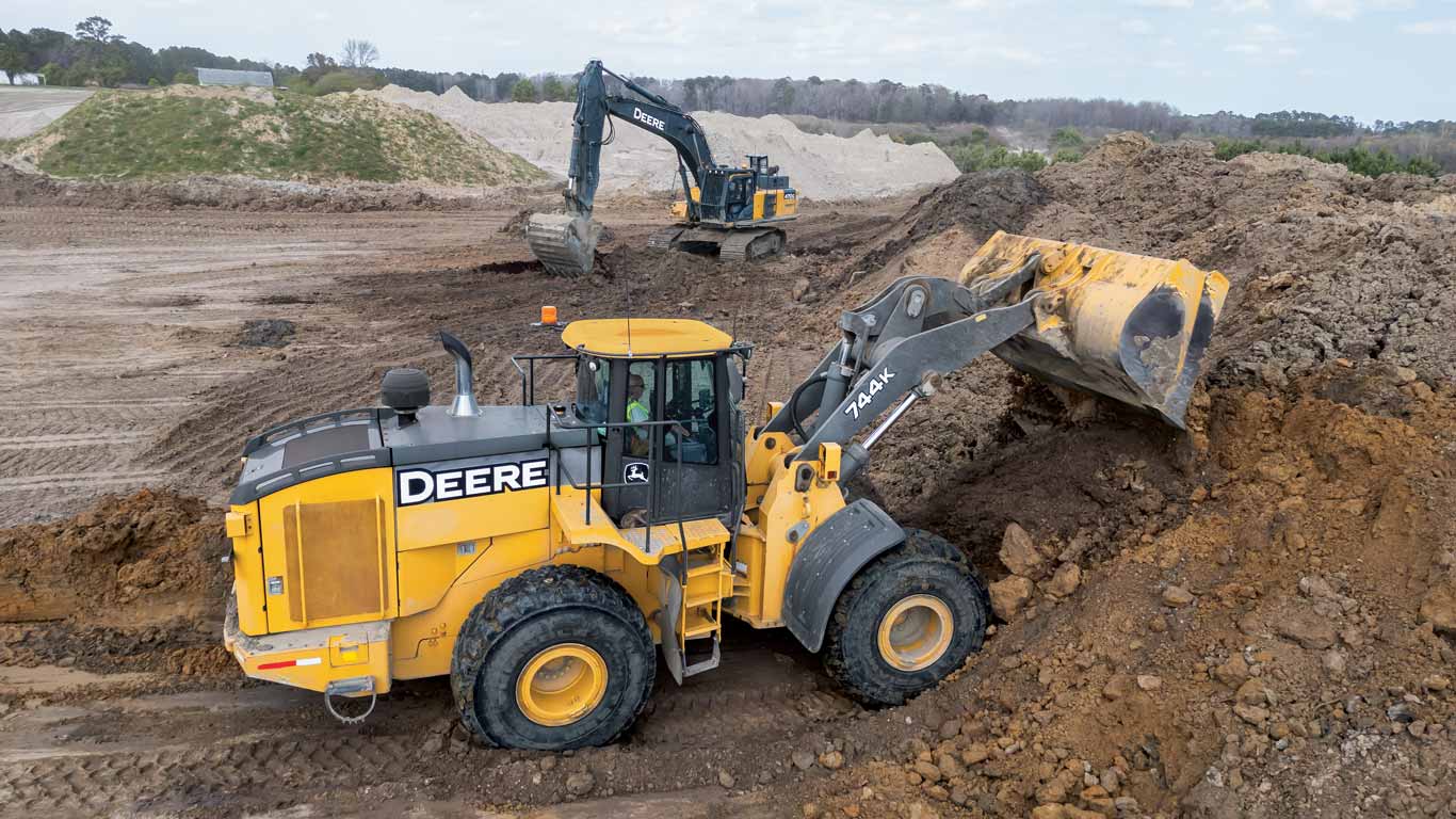 Two Deere construction vehicles moving dirt on a large, open construction site.
