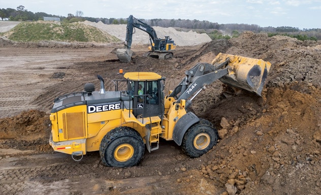 Two Deere construction vehicles moving dirt on a large, open construction site.