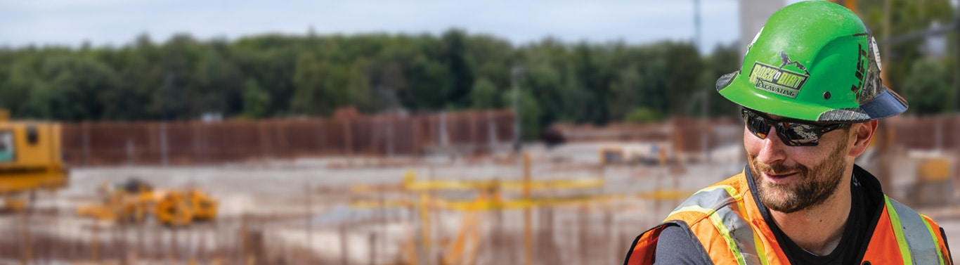 Worker in green hard hat and orange vest at construction site.