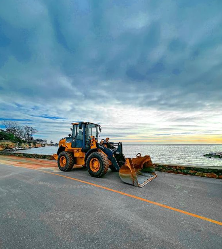 A John Deere 444 wheel loader on a lakefront road at sunset. 