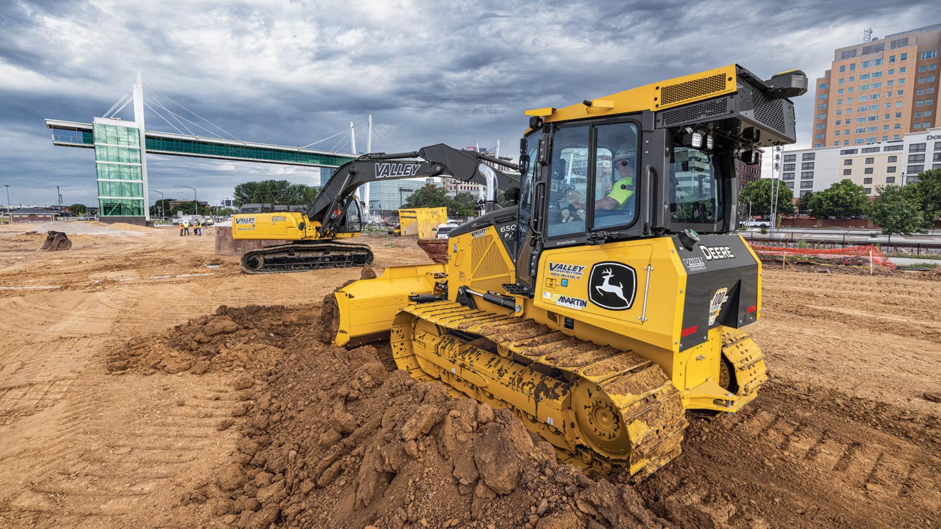 A John Deere 350 G-Tier Excavator digs dirt and a 650 P-Tier moves the mount to level and grade the dirt.