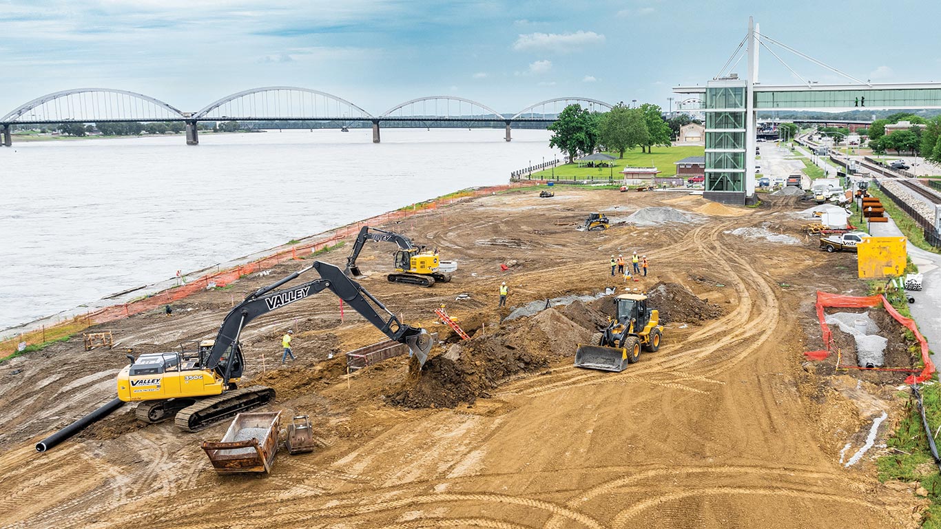 A John Deere 350 G-Tier Excavator scoops and piles it up, getting the area ready for drainage pipe installation.