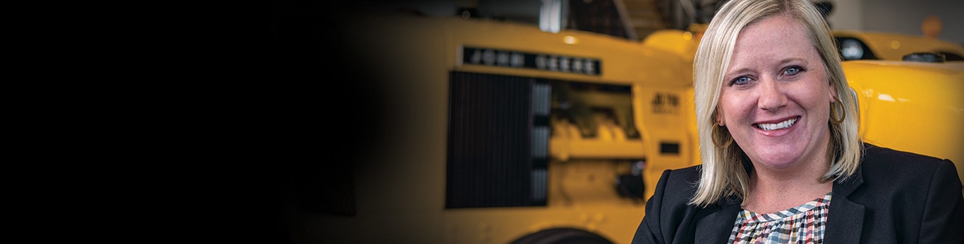 Lauren Coffaro standing in front of two antique John Deere construction tractors.