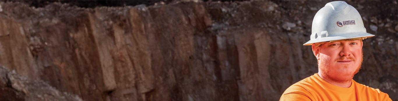Smiling construction worker with white hardhat on standing in front of a rock face