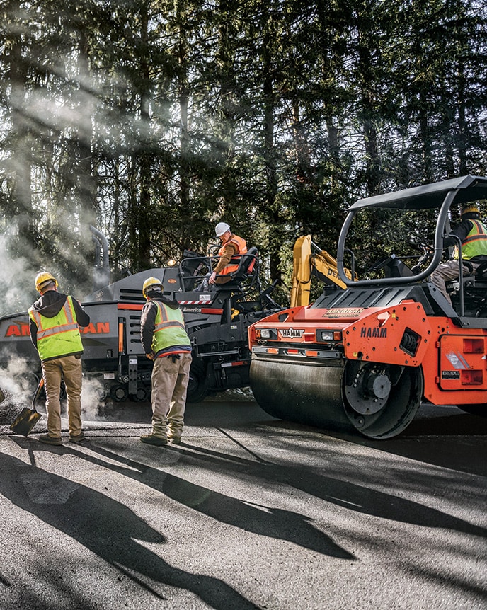 The crew utilize a John Deere 324G Skid Steer, HAMM HD 70 Tandem Rollers, and a VÖGELE Road Paver on an asphalt paving job.