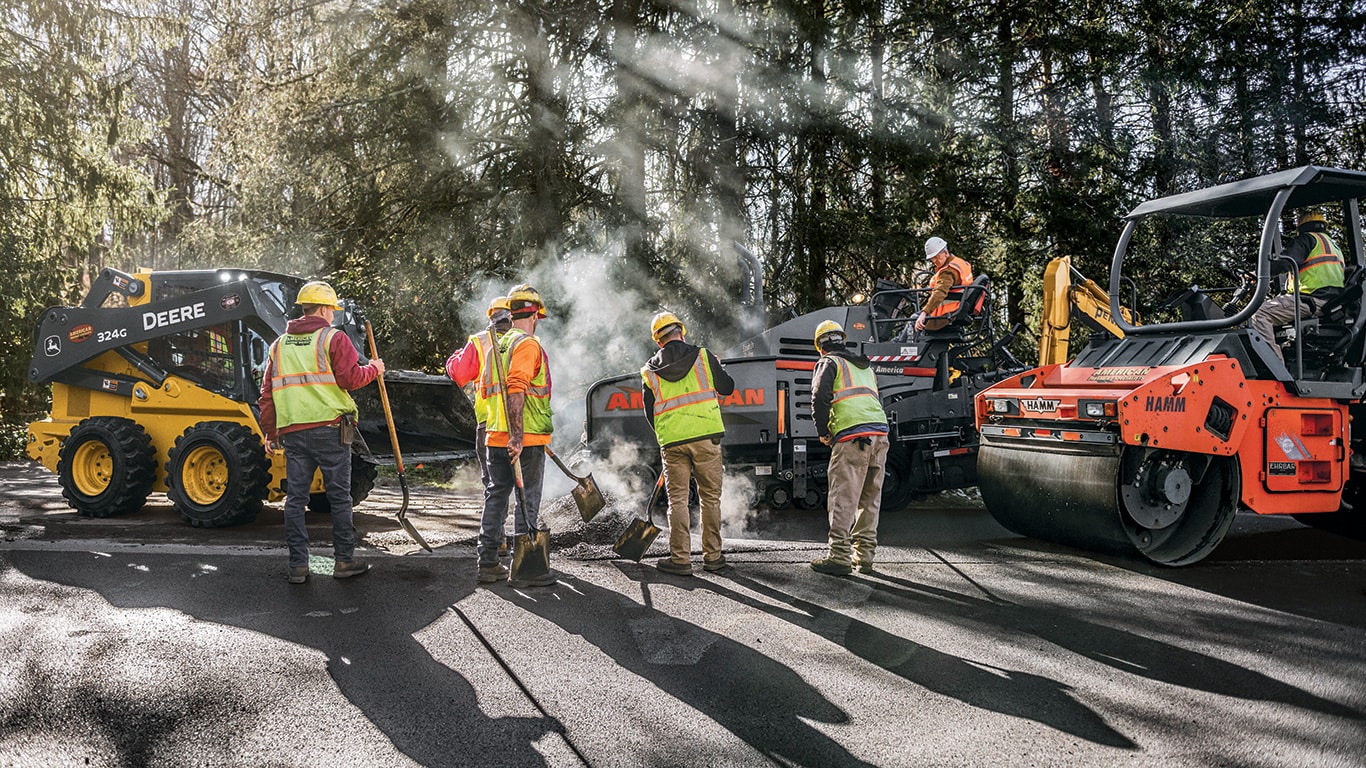 The crew utilize a John Deere 324G Skid Steer, HAMM HD 70 Tandem Rollers, and a VÖGELE Road Paver on an asphalt paving job.