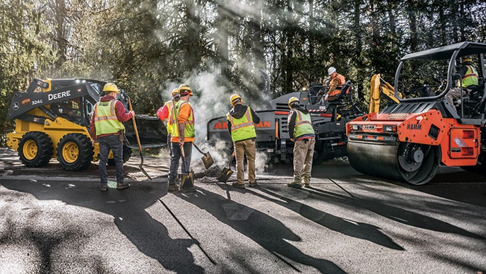 The crew utilize a John Deere 324G Skid Steer, HAMM HD 70 Tandem Rollers, and a VÖGELE Road Paver on an asphalt paving job.