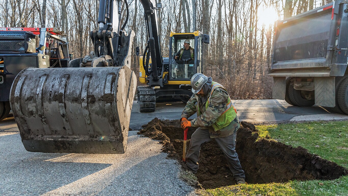 Michael Flaherty operates a John Deere 85G Excavator as Jacob Pepin prepares the hole for the shoring box.