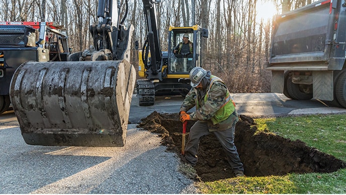 Michael Flaherty operates a John Deere 85G Excavator as Jacob Pepin prepares the hole for the shoring box.