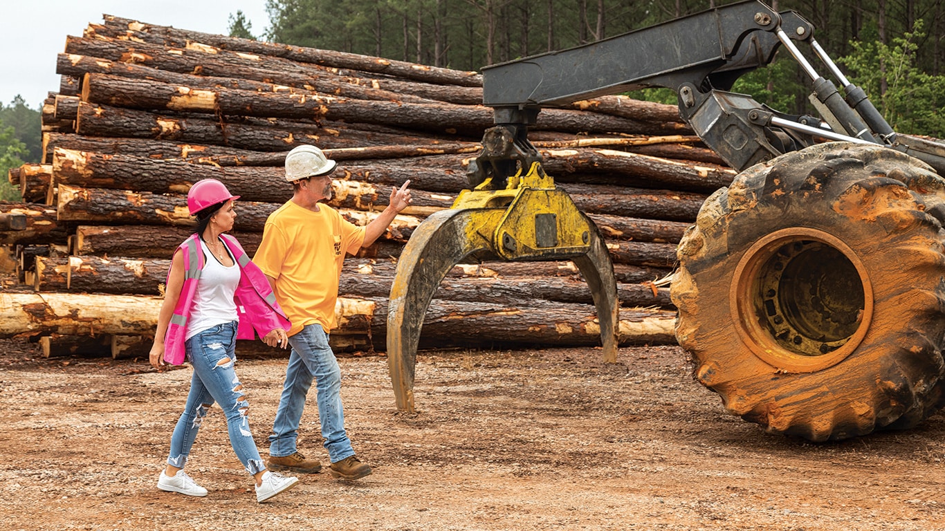 Samantha Bull and Tad Ward walk across the landing site in front of a parked 648L Grapple Skidder.