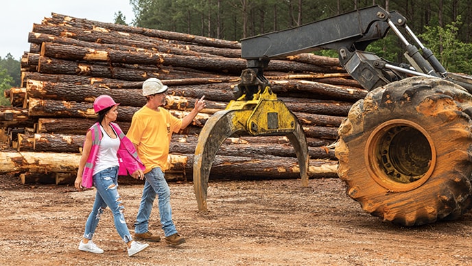 Samantha Bull and Tad Ward walk across the landing site in front of a parked 648L Grapple Skidder.