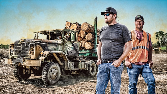 Ron and Rusty Delk of R&R Swamp Logging stand at a landing site with a logging truck behind them.