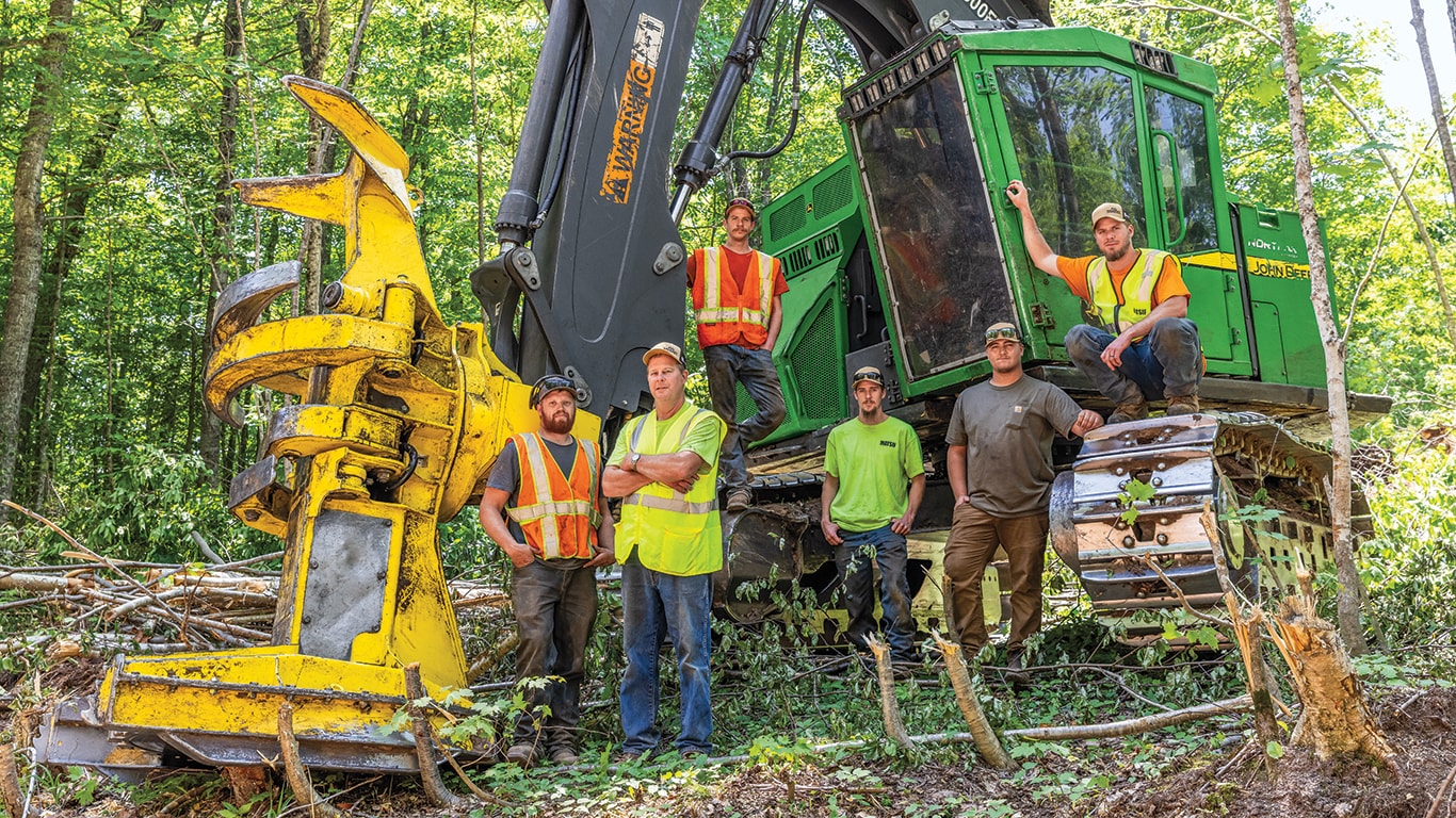 Standing within the Michigan woods, Max Tervo, Doug Anderson, Ladd Anderson, Nash Anderson, Eli Larson, and Dane Anderson, all of Doug Anderson Logging, stand beside an 853M Tracked Feller Buncher.