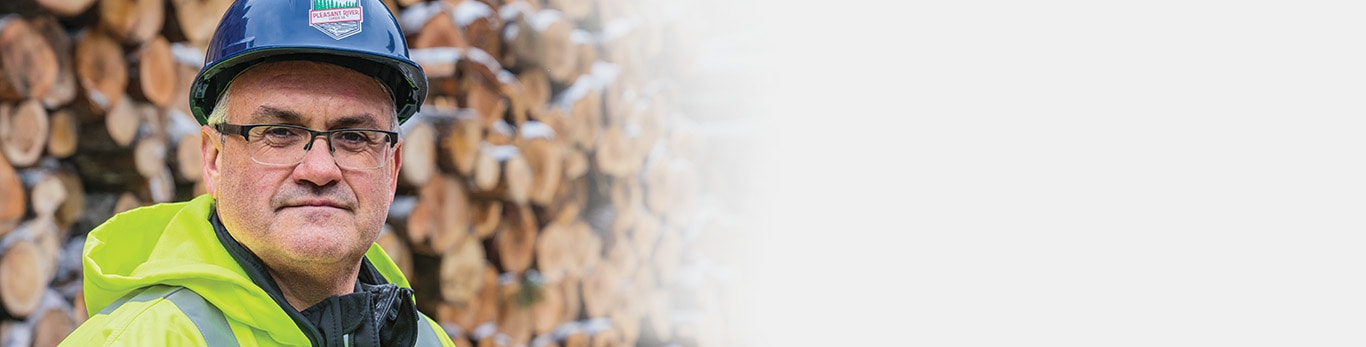 Jason Brochu poses in front of snow-covered logs at the sawmill. 