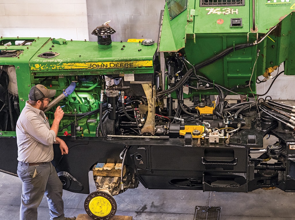 Standing beside a grapple skidder, Jordan Everhart is checking out the engine area with a flashlight.