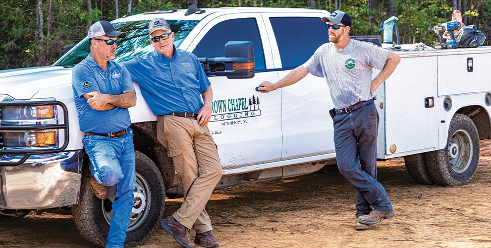 Randy Wilkes, Dobbs Equipment dealer representative, talks with father and son owners Bud West of Brown Chapel Logging and Matt West of West Forest Products.