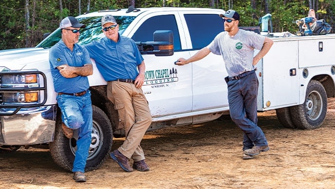 Randy Wilkes, Dobbs Equipment dealer representative, talks with father and son owners Bud West of Brown Chapel Logging and Matt West of West Forest Products.