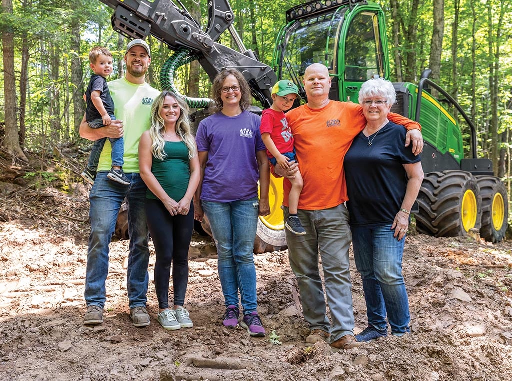Multiple generations of the Harju family stand together in a forest beside a 1270G Wheeled Harvester.