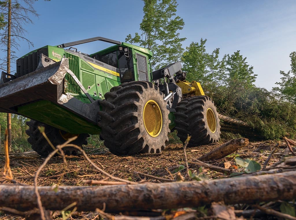 A 748L-II Skidder drags whole trees within its grapple through a forest.