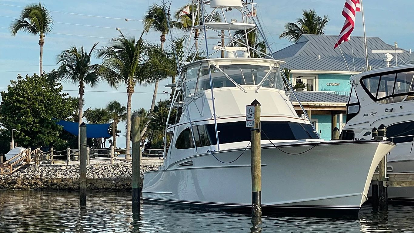 A newly repowered 54-foot Rybovich sportfishing yacht docked at shore with palm trees and a building in the background