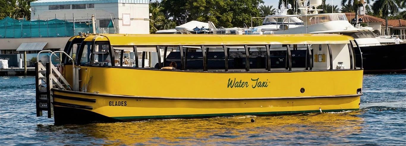 A gold water taxi named ‘Glades’ floating in a harbor on a sunny day.