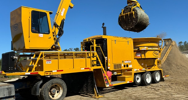 Jones Manufacturing Mighty Giant grinder, powered by a John&nbsp;Deere JD18 engine, lifting a hay bale into a grinder. 